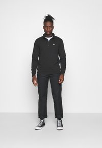 Black quarter-zip sweatshirt with ribbed cuffs and hem, paired with black cropped pants and black high-top sneakers.