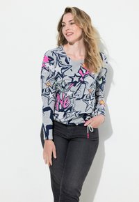 Graues langärmliges Oberteil mit bunten Sternmustern und rosa sowie neon Akzenten. Kombiniert mit dunkelblauen Jeans, umfasst das Outfit ein Kordelzugdetail.