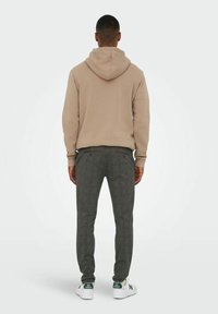 Beige hoodie, grijs geblokte broek en witte sneakers met groene accenten. Zicht van achteren, toont casual outfitsamenstelling.