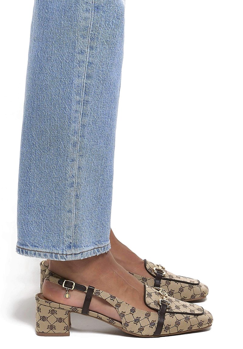 Pieds portant des chaussures slingback à talons blocs beiges à motifs, associées à un jean en denim bleu clair coupé au-dessus de la cheville.