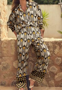 Chemise boutonnée et pantalon assorti avec un motif noir, blanc et jaune. Coupe décontractée, tissu doux, présentant des motifs géométriques audacieux et des finitions contrastées.