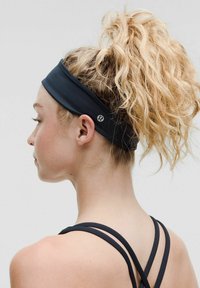 Sort atletisk hårbånd lavet af strækbart materiale, designet med en glat overflade og med et logo på siden.