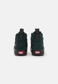 Grønne suedhøje sneakers med sorte accenter, gummisåler og bageste trækflapper. Har et rødt Vans-logo ved hælen.