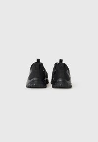 Zwarte sportschoenen met een geprofileerde bovenkant, rubberen buitenzool en trekkoorden bij de hiel. Kenmerkt zich door een strakke, minimalistische uitstraling.