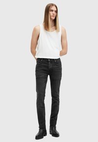 Schwarze Denim-Jeans mit schlanker Passform, die über ein Fünf-Taschen-Design und minimale Abnutzungserscheinungen verfügen. Kombiniert mit einem ärmellosen weißen Shirt.