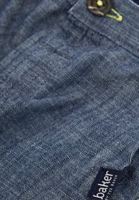 Jeans i en mörkblå nyans med en strukturerad tyg, med knappstängning och en liten märkesetikett på sidan.