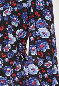 Tissu noir avec des motifs floraux bleus et blancs et de petits accents rouges, présentant un détail de nœud en tissu noué.
