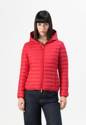 Rode pufferjack met capuchon, met horizontale gestikte lijnen, rits aan de voorkant met oranje trekker en elastische manchetten, gedragen over donkerblauwe jeans.