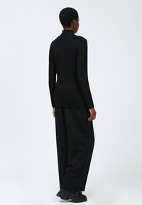 Schwarzes langärmliges Rollkragenoberteil aus einem glatten Stoff, kombiniert mit lockeren schwarzen Hosen und schwarzen klobigen Stiefeln.