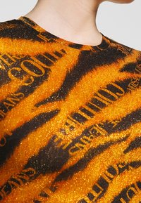 Zbliżenie osoby noszącej błyszczącą bluzkę w tigrze paski z rozrzuconymi czarnymi napisami na pomarańczowej i czarnej tkaninie.