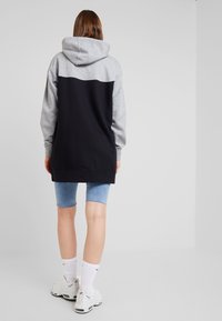 Sudadera con capucha, parte superior gris y parte inferior negra, confeccionada con tela suave. Combinada con pantalones cortos de mezclilla y zapatillas blancas con detalles en negro.
