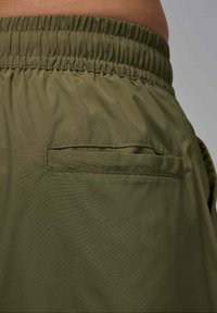 Vihreät shortsit, joissa on joustava vyötärönauha ja litteä takatasku. Kangas on sileä ja kevyt, mattapintainen.