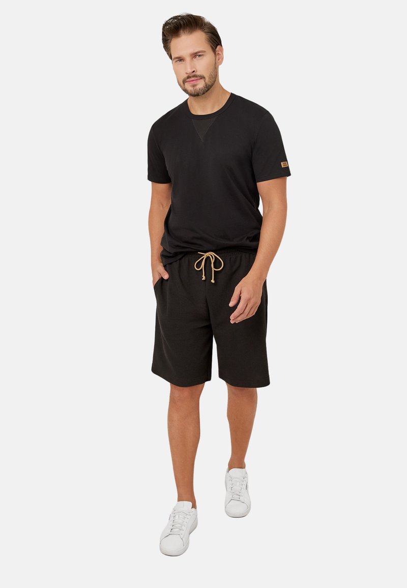 Czarna koszulka z krótkim rękawem i okrągłym dekoltem, z detalem w kształcie litery V. Połączona z czarnymi szortami z elastycznym pasem i brązowym sznurkiem.