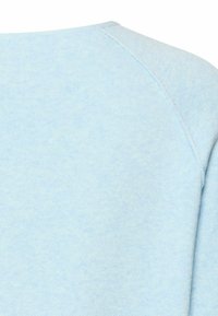 Light blue fabric with visible stitching detail near shoulder seam, showing texture and soft knit material.