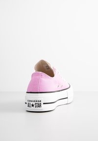 Rosa canvass lågskor med vit gummisula, svart rand och präglad "CONVERSE ALL STAR"-logotyp på hälen. Har metallöglor.