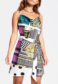 Vestido multicolorido con una mezcla de patrones que incluye estampado animal, rayas y lunares; cintura ceñida con un lazo, textura suave.