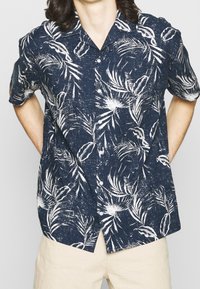 Navy short-sleeve button-up shirt with a white tropical leaf print; lightweight fabric with a textured finish, featuring a classic collar.