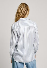 Chemise à rayures à manches longues en bleu clair et blanc, avec un col boutonné, une coupe décontractée et un ourlet arrondi avec des fentes sur les côtés.