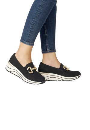 Zwarte instapschoenen met een suède textuur, voorzien van gouden accenten en een dikke witte platformzool met een zigzagpatroon.