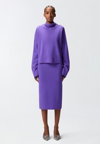 Maglione viola a maglia con un alto colletto a coste, taglio corto e maniche larghe, abbinato a una gonna viola al ginocchio e tacchi decorati.