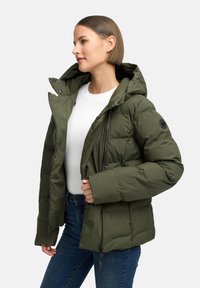 Olivinės spalvos pūkinė striukė su gobtuvu, turinti užtrauktuką, šonines kišenes, siuvinėtą tekstūrą ir apvalų logotipą ant kairiojo rankovės.