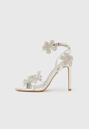 Silver high-heeled sandal featuring floral embellishments with rhinestones, a slender ankle strap, and an open-toe design.