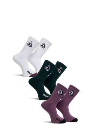Trois paires de chaussettes mi-mollet en blanc, vert foncé et violet, chacune avec un logo géométrique noir et blanc et un texte "VOLCOM" près des orteils.