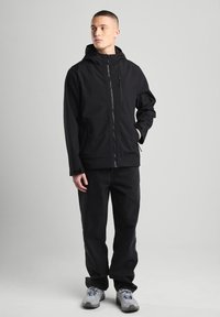 Black hooded jacket with zip closure and side pockets, paired with black pants and grey sneakers. Smooth texture, minimalistic design.