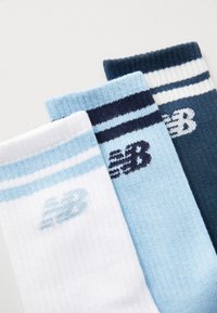 Tre par stickade strumpor: vita med ljusblå ränder, ljusblå med mörkblå ränder och mörkblå med vita ränder, som har New Balance-logotypen.