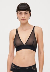 Black bralette with a sheer mesh upper and solid band. Features a deep V-neck design and thin adjustable straps.