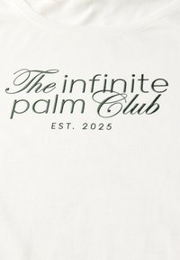 T-shirt en coton blanc avec du texte vert : "The infinite palm Club EST. 2025", avec une police élégante et un col rond.