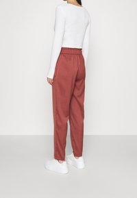 Roestkleurige pantalons met een elastische tailleband, licht toelopende pijpen en voorzakken, gecombineerd met een aansluitend wit longsleeve shirt.