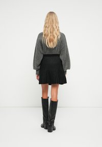 Pull en maille texturée gris avec des manches ballons, associé à une jupe plissée noire à rayures verticales blanches et des bottes noires jusqu'aux genoux.