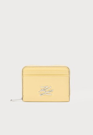 Portefeuille en cuir jaune avec logo embossé, fermeture éclair et plusieurs fentes pour cartes. Texture lisse et coutures soignées. Forme rectangulaire compacte.