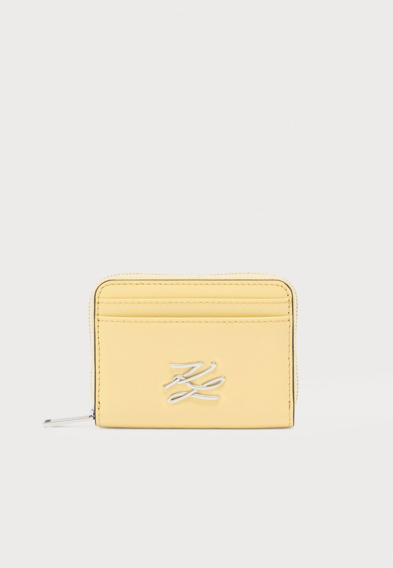 Portefeuille en cuir jaune avec logo embossé, fermeture éclair et plusieurs fentes pour cartes. Texture lisse et coutures soignées. Forme rectangulaire compacte.