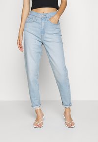 Ljusblå högmidjade jeans med avslappnad passform, inklusive framfickor och uppvikta fållar. Matchas med vita sandaletter med remmar.