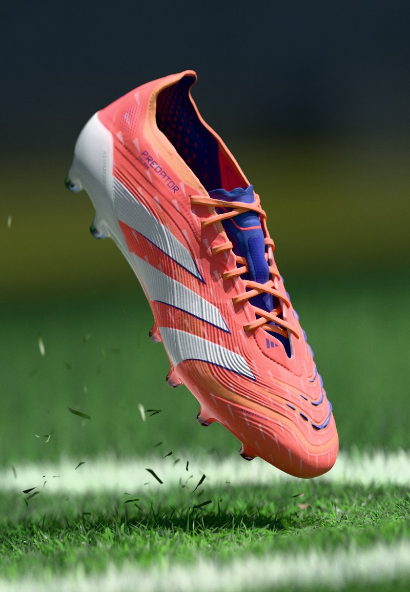 Botas de fútbol naranjas y blancas con una superficie texturizada, que presentan un forro interior azul y cordones en contraste, flotando sobre césped verde.