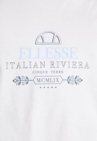 Bílé bavlněné tričko s textem "ELLESSE ITALIAN RIVIERA" v modré a černé barvě, s dekorativními detaily a grafickým logem nad ním.