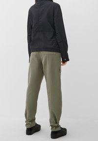 Veste légère noire avec col montant, associée à un pantalon cargo vert olive avec poches latérales et poignets à cordon, portée avec des baskets noires.