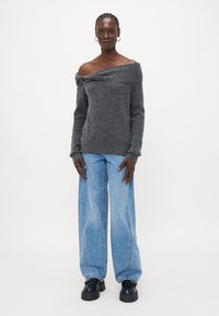 Grå strikkegenser med avtagne skuldre og myk tekstur, kombinert med lyseblå vide jeans og svarte sko med kraftig såle.