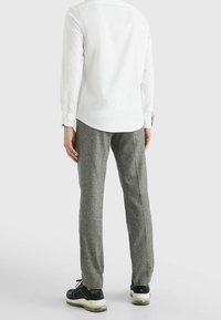 Wit lang mouwshirt met een afgeronde zoom. Grijze textuurbroek. Zwarte sneakers met lichte zolen. Minimalistisch ontwerp, geen patronen of accenten.