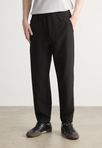 Pantalons ajustés noirs avec une taille élastique, des poches avant et des détails de cordon contrastés. Fabriqués dans un tissu doux et offrant une coupe décontractée.