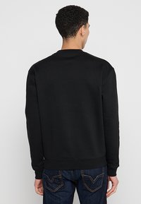 Felpa nera in cotone con maniche lunghe, scollatura a girocollo e orlo a coste. Indossata da un modello, presenta una texture liscia e nessun logo visibile.