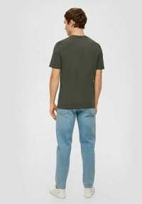 Olivgrünes Baumwoll-T-Shirt mit kurzen Ärmeln, Rundhalsausschnitt und lässiger Passform, kombiniert mit hellblauen Jeans und weißen Sneakers.