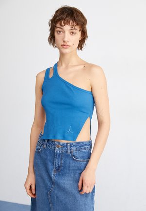 Top corto azul de canalé con diseño de un solo hombro y corte lateral. Presenta un pequeño logo en el dobladillo. Combinado con una falda de mezclilla de cintura alta.