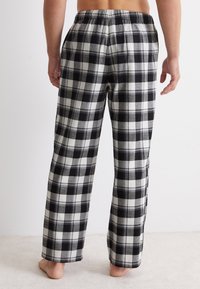 Svart och vit rutiga pyjamasbyxor med elastisk midja, avslappnad passform och mjuk tygtextur. Utsikt från baksidan som visar hel längd design.
