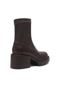 Botines de cuero marrón con tacón ancho, textura lisa, puntera redondeada y costuras visibles a lo largo del borde superior y la suela.