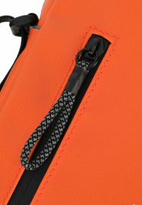 Oranžová voděodolná taška s texturovaným povrchem, vybavená zipovým uzávěrem, černým táhlem a kontrastním černým prošíváním podél okrajů.