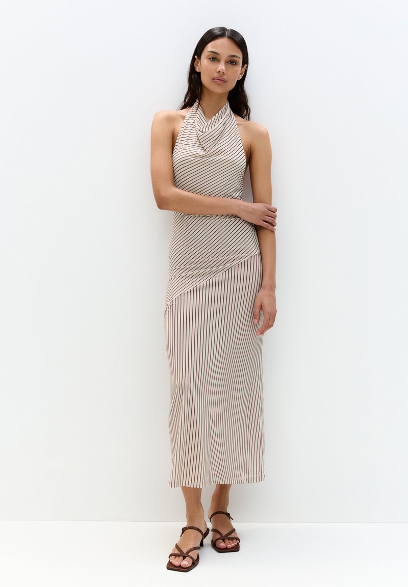 Halterneck-Kleid in Beige mit karminroten vertikalen Streifen. Slim Fit, knielang, aus leichtem Stoff, dezente Drapierung, kombiniert mit braunen Riemchensandalen.