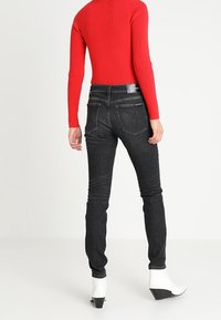 Svarta tajta jeans med bakfickor, hög midja och lätt stretch. Kombination med en åtsittande röd ribbad topp och vita ankelstövlar.